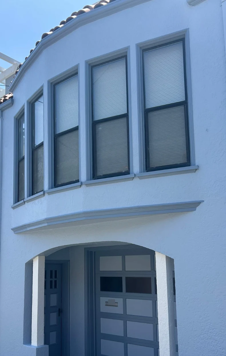 The same house after painting, with light blue stucco and gray window trim